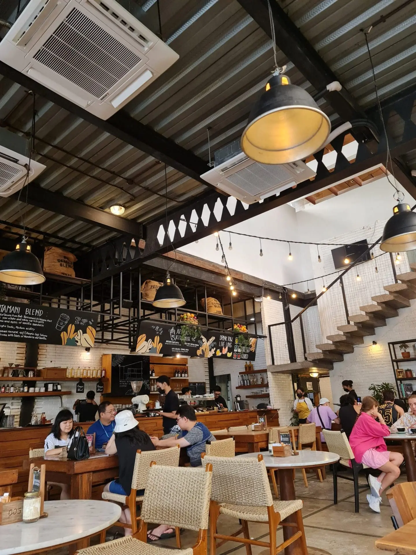 Photo of Interior view of a café featuring wooden tables and chairs, with decorative lighting and a staircase. | Wander Sober