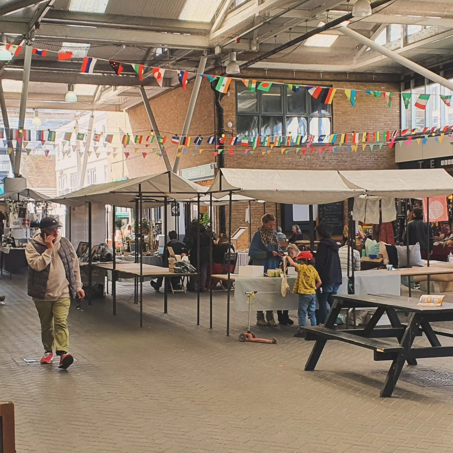 Photo of View of an indoor market featuring various stalls and colorful flags hanging from the ceiling. | Wander Sober