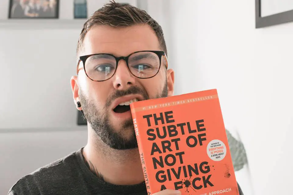 Photo of Person holding 'The Subtle Art of Not Giving a F*ck' book while making a facial expression. | Wander Sober
