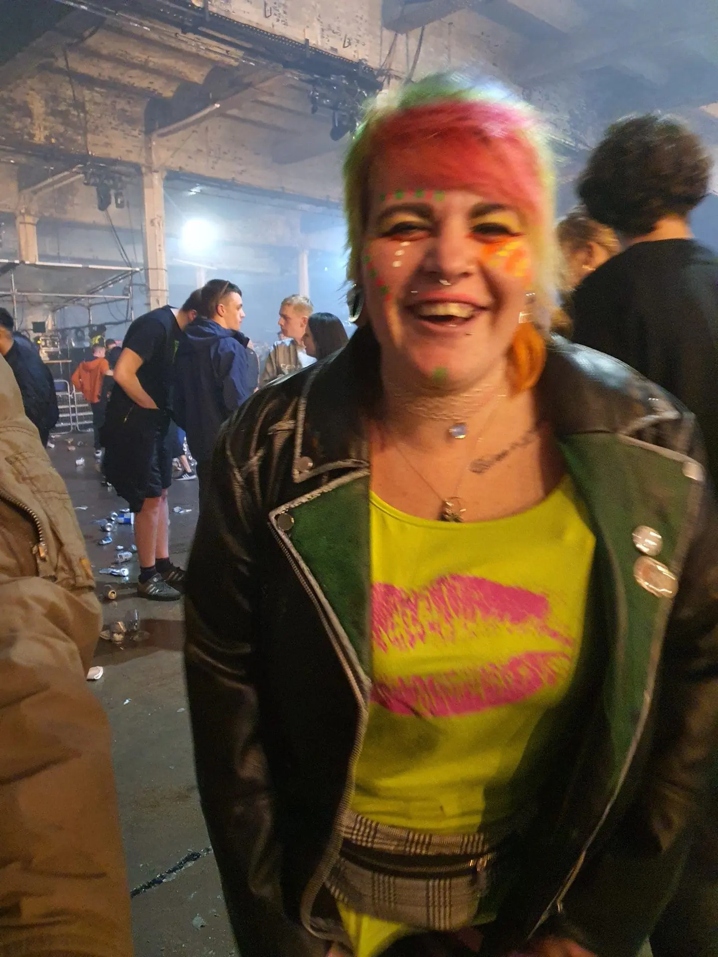 Photo of Individual with vibrant hair and face paint smiling at an indoor event. | Wander Sober