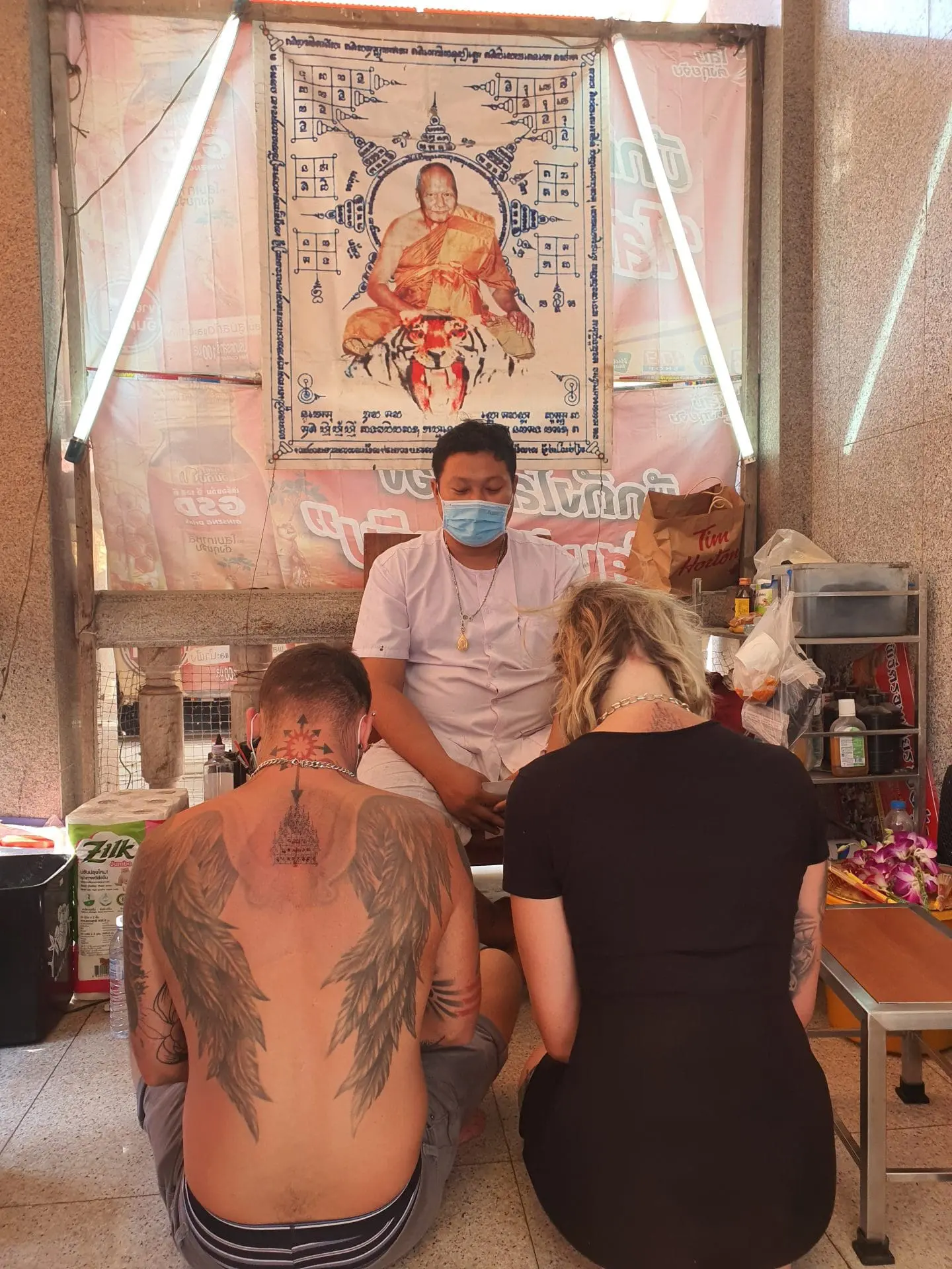 Photo of Two individuals sitting in front of a tattoo artist in a studio with a portrait in the background. | Wander Sober