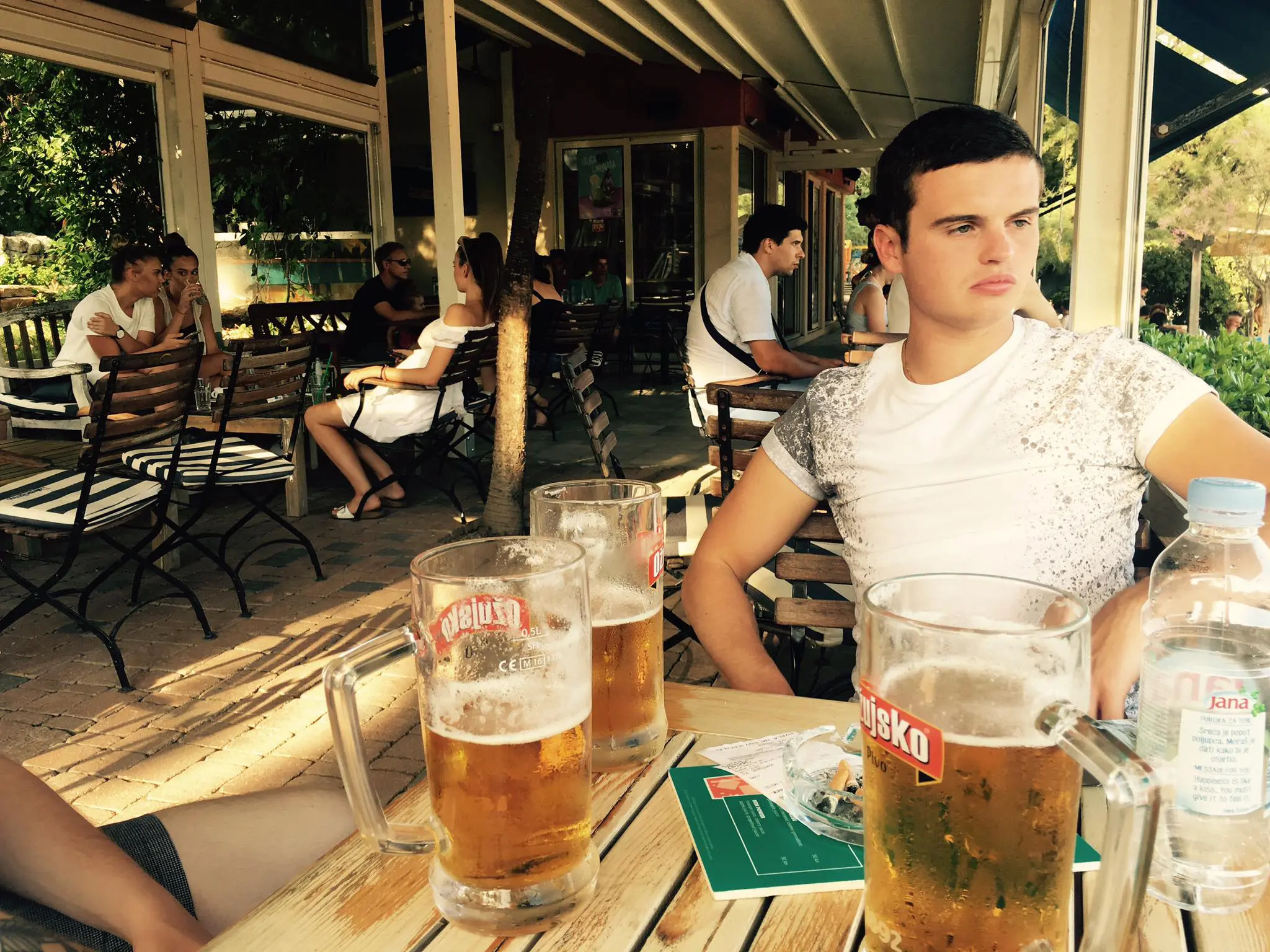 Photo of A young man sitting at a table with several mugs of beer in a casual outdoor setting. | Wander Sober