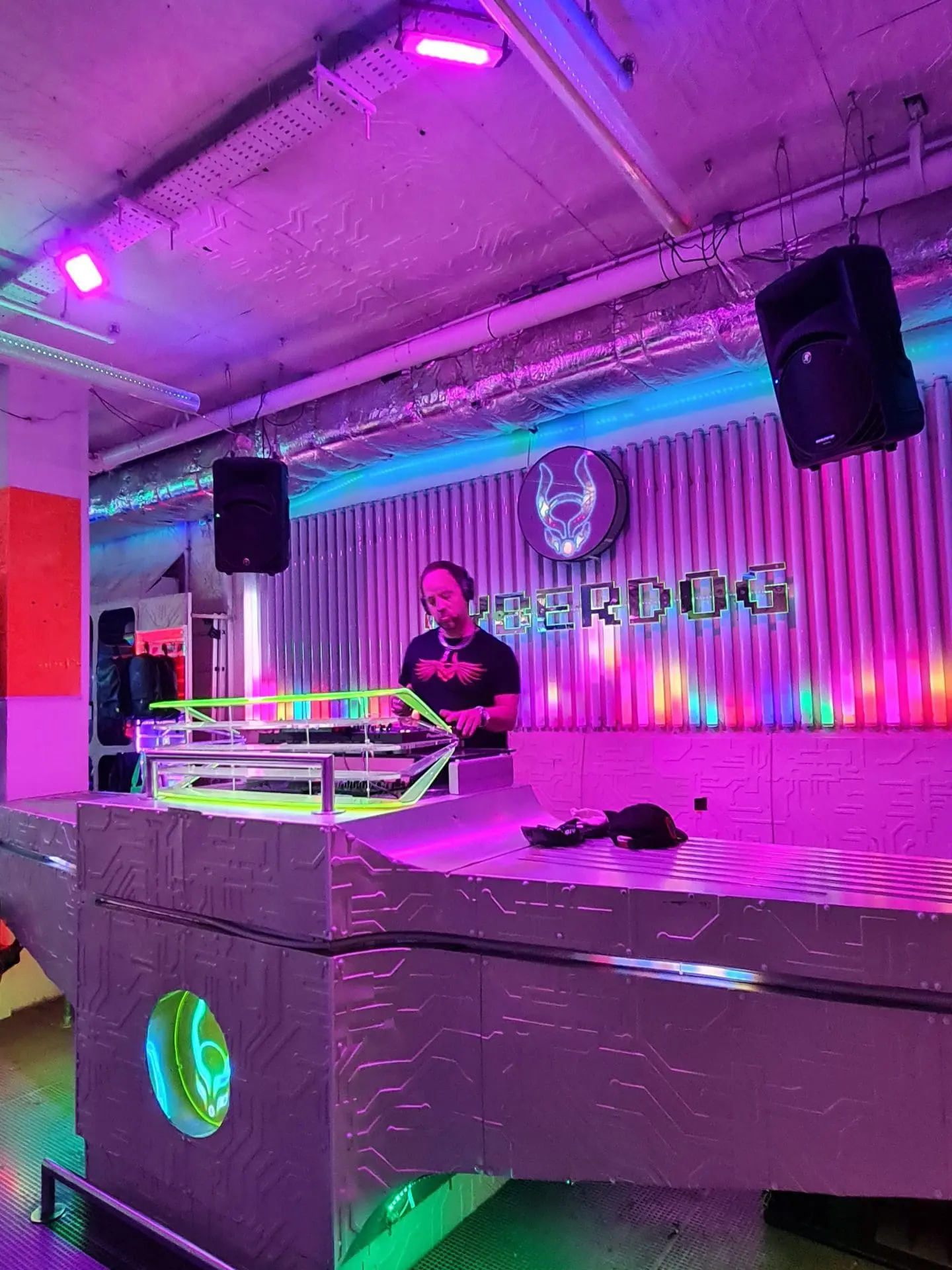 Photo of DJ standing behind a neon-lit DJ booth with colorful lighting in a nightclub setting. | Wander Sober