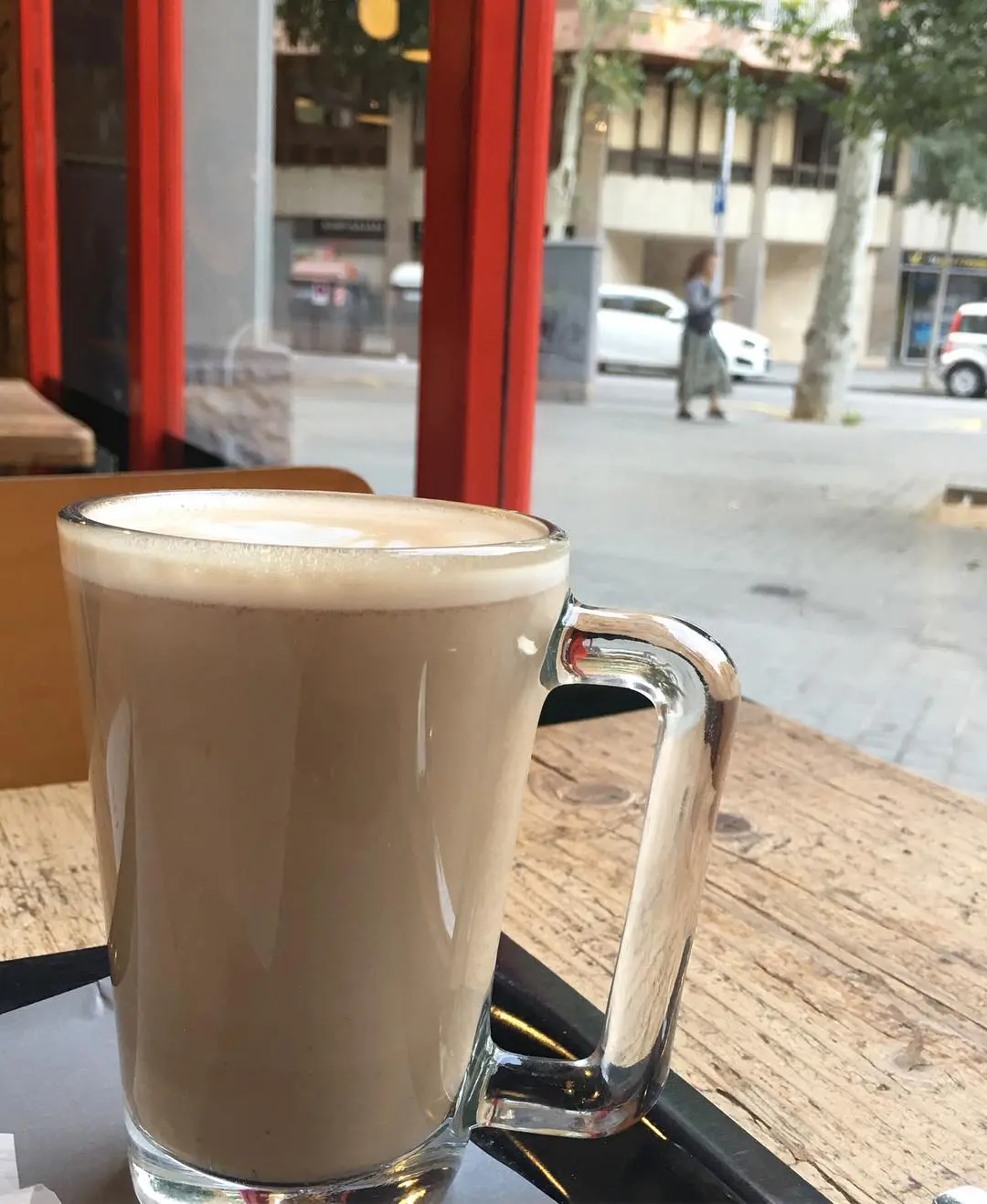 Photo of A glass of latte with a frothy top placed on a wooden table near a window. | Wander Sober