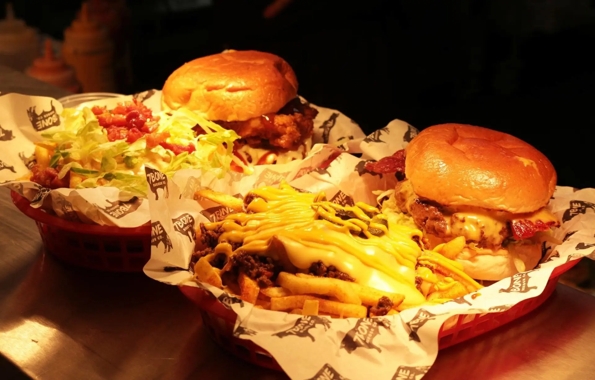 Photo of Two burgers with cheese and a side of fries topped with cheese in red baskets. | Wander Sober