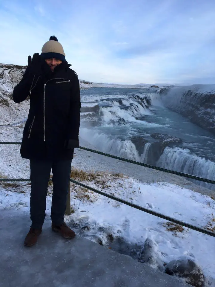 Photo of Individual wearing winter clothing standing near Gullfoss Waterfall in Iceland during winter. | Wander Sober