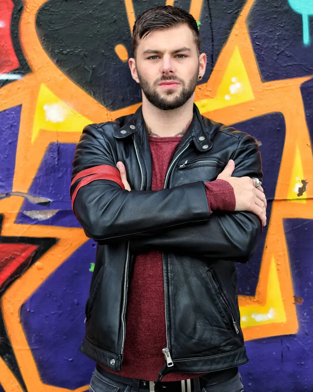 Photo of A man wearing a black leather jacket with arms crossed, standing in front of a colorful graffiti wall. | Wander Sober