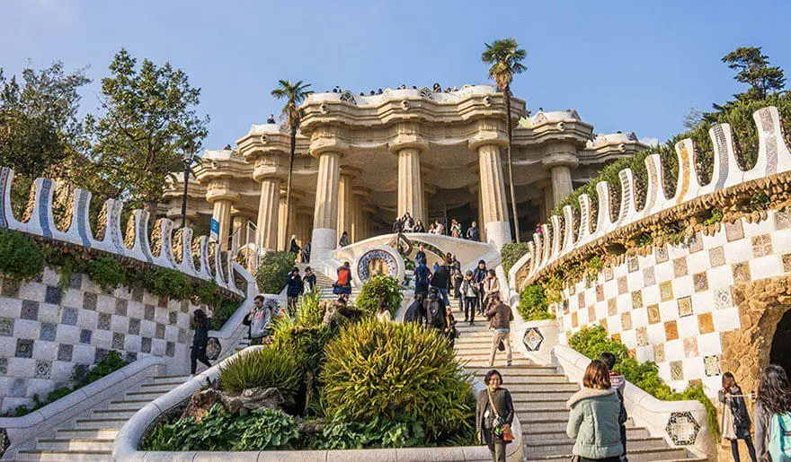 Entrance to Park Güell featuring mosaic steps and a large architectural structure with columns.
