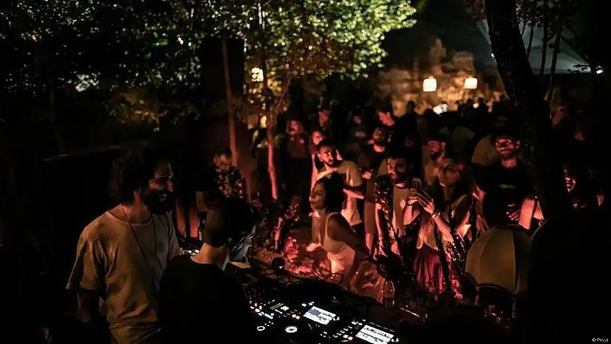 Photo of A DJ performing in front of a crowd at an outdoor event with dim lighting and trees in the background. | Wander Sober