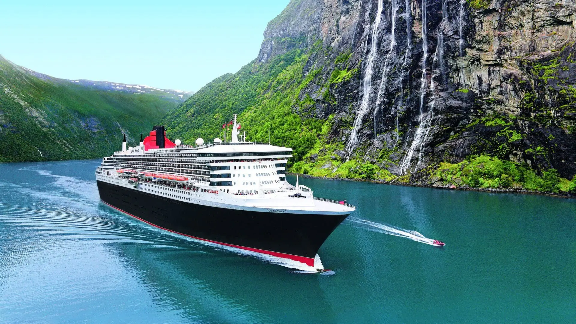 Photo of Large cruise ship navigating through a fjord surrounded by steep green cliffs and a waterfall. | Wander Sober