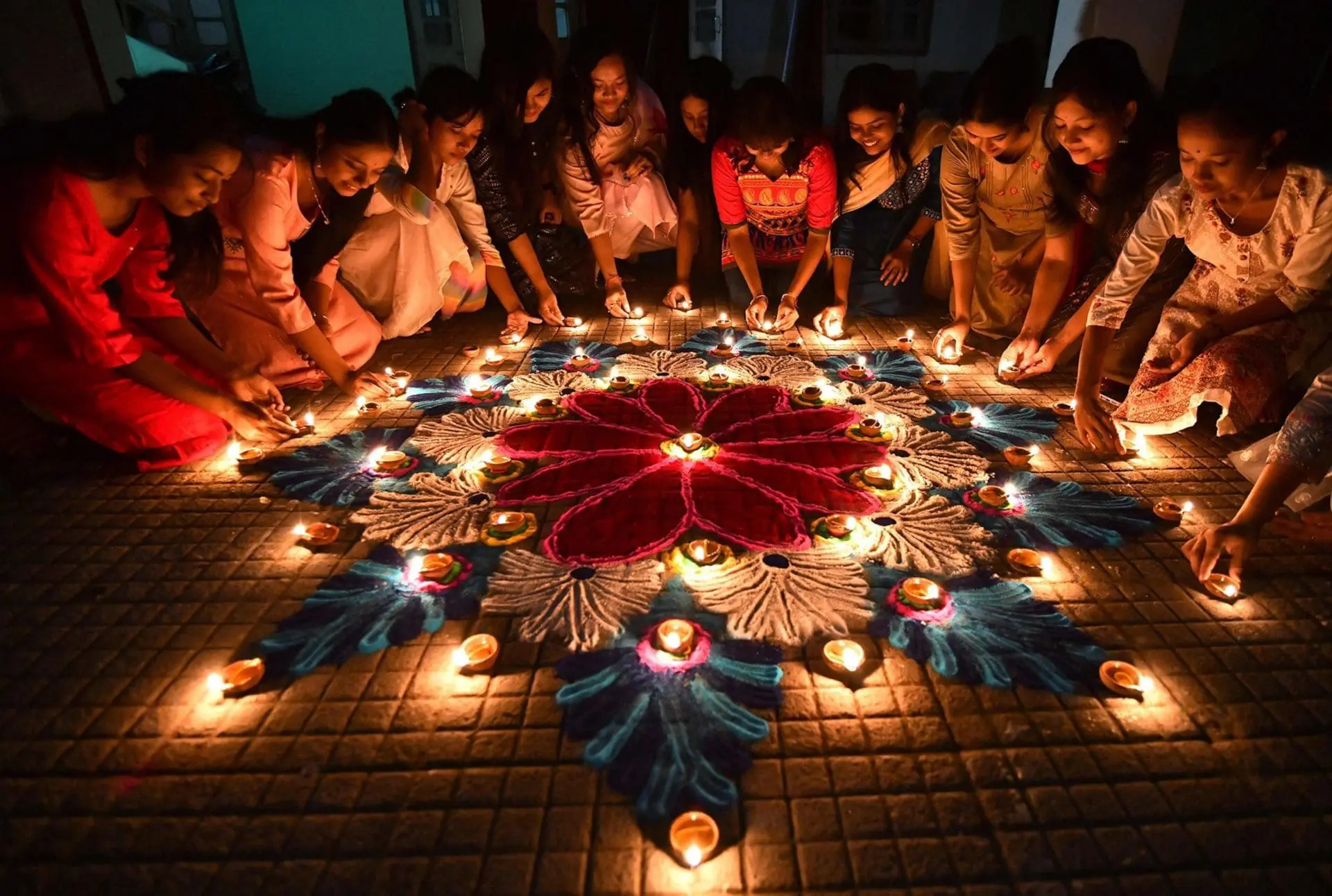 Group of individuals arranging diyas around a colorful rangoli design on the ground.