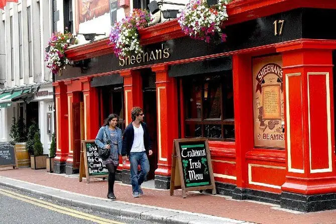Photo of Exterior view of Sheehan's pub featuring red walls, flower baskets, and signage on the street. | Wander Sober