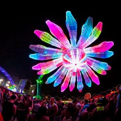 Photo of Large illuminated flower-shaped installation with vibrant colors at a nighttime event. | Wander Sober