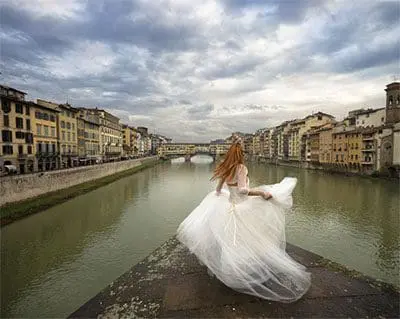 Photo of Woman wearing a flowing white dress standing by the Arno River in Florence, Italy. | Wander Sober