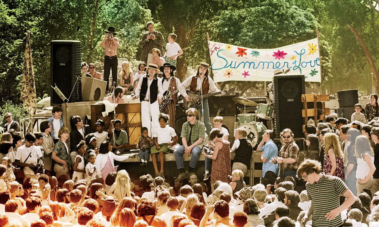 Photo of A large crowd gathered around a stage with musicians performing at a Summer of Love event. | Wander Sober