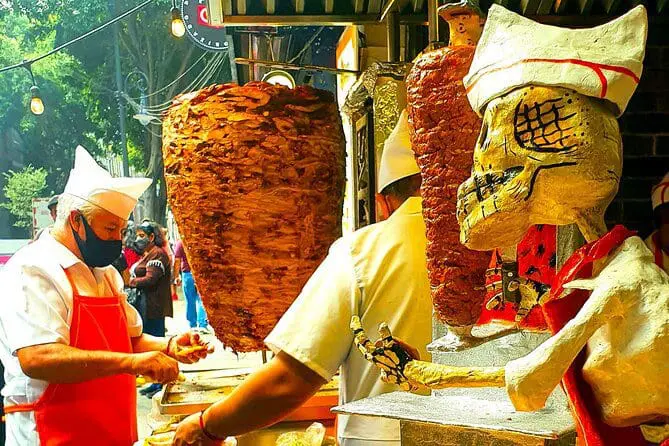Photo of Street food vendor preparing tacos with a large vertical spit of meat in the background. | Wander Sober