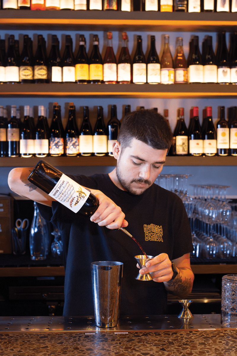 Photo of Bartender pouring liquid from a bottle into a jigger at a bar counter. | Wander Sober