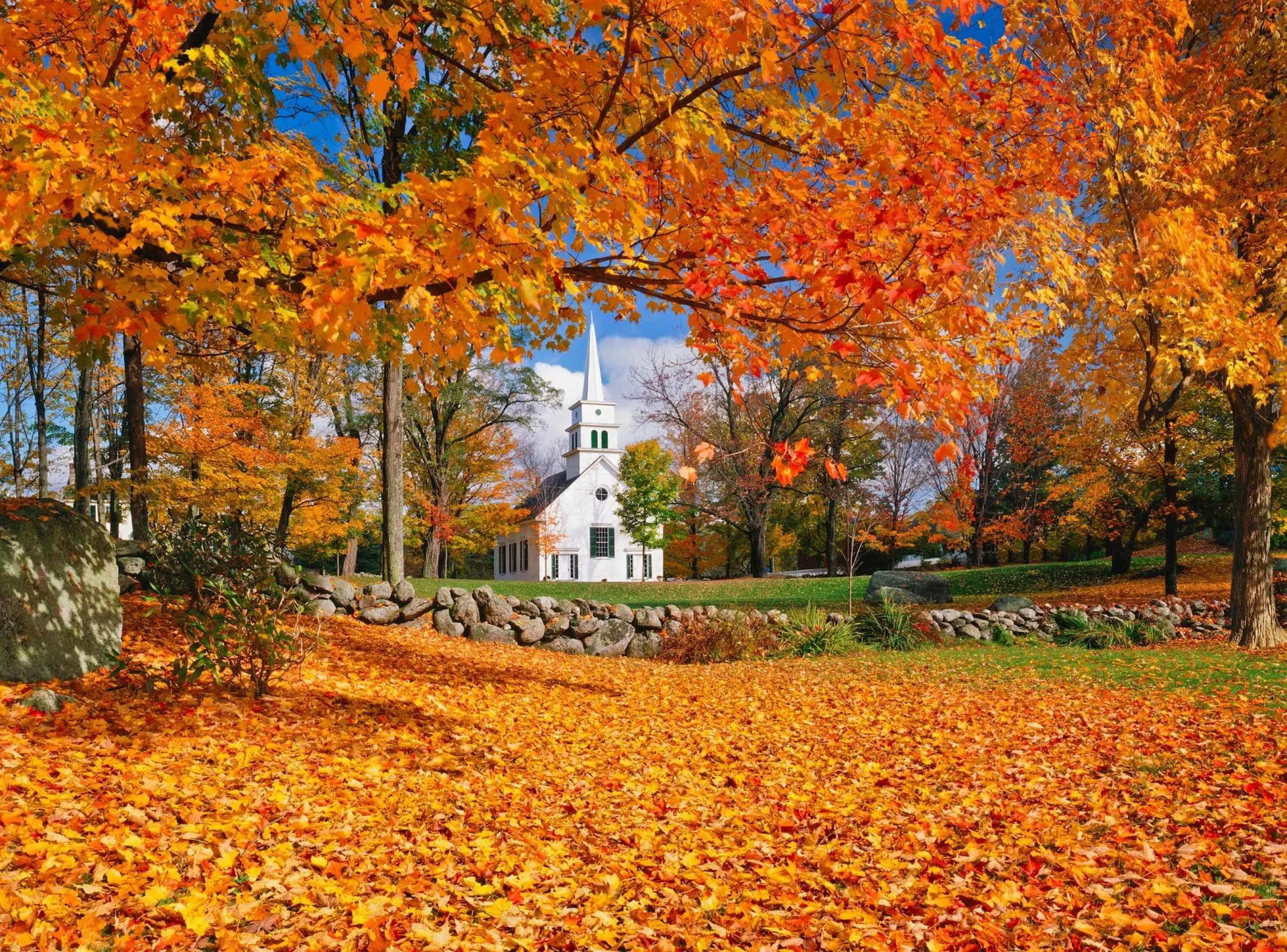Photo of A white church with a steeple set against vibrant autumn trees and fallen leaves. | Wander Sober
