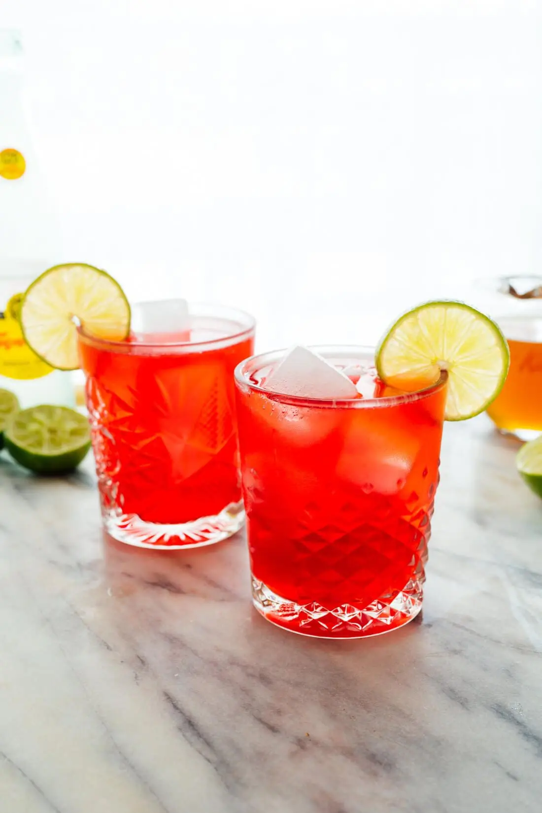 Photo of Two crystal glasses filled with a red cocktail garnished with lime slices and ice cubes. | Wander Sober