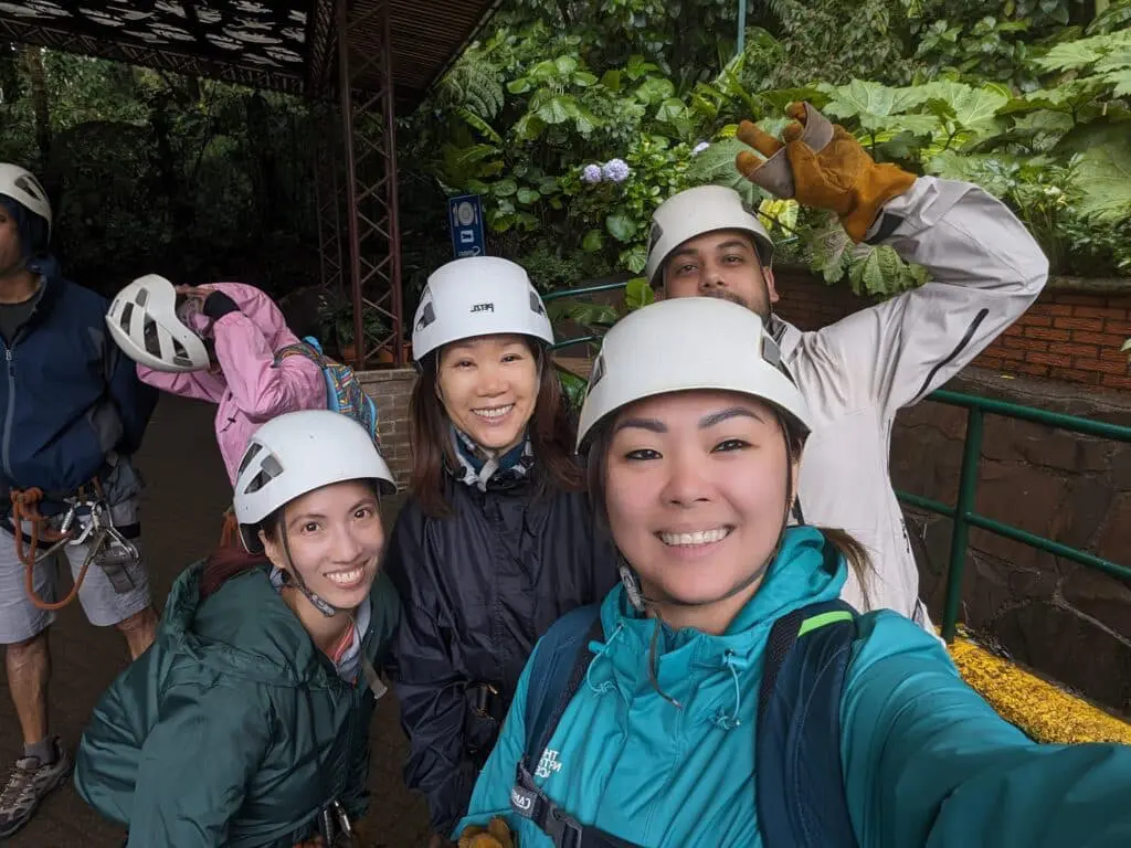 Photo of Four individuals wearing helmets and safety gear, posing for a selfie in a lush green environment. | Wander Sober
