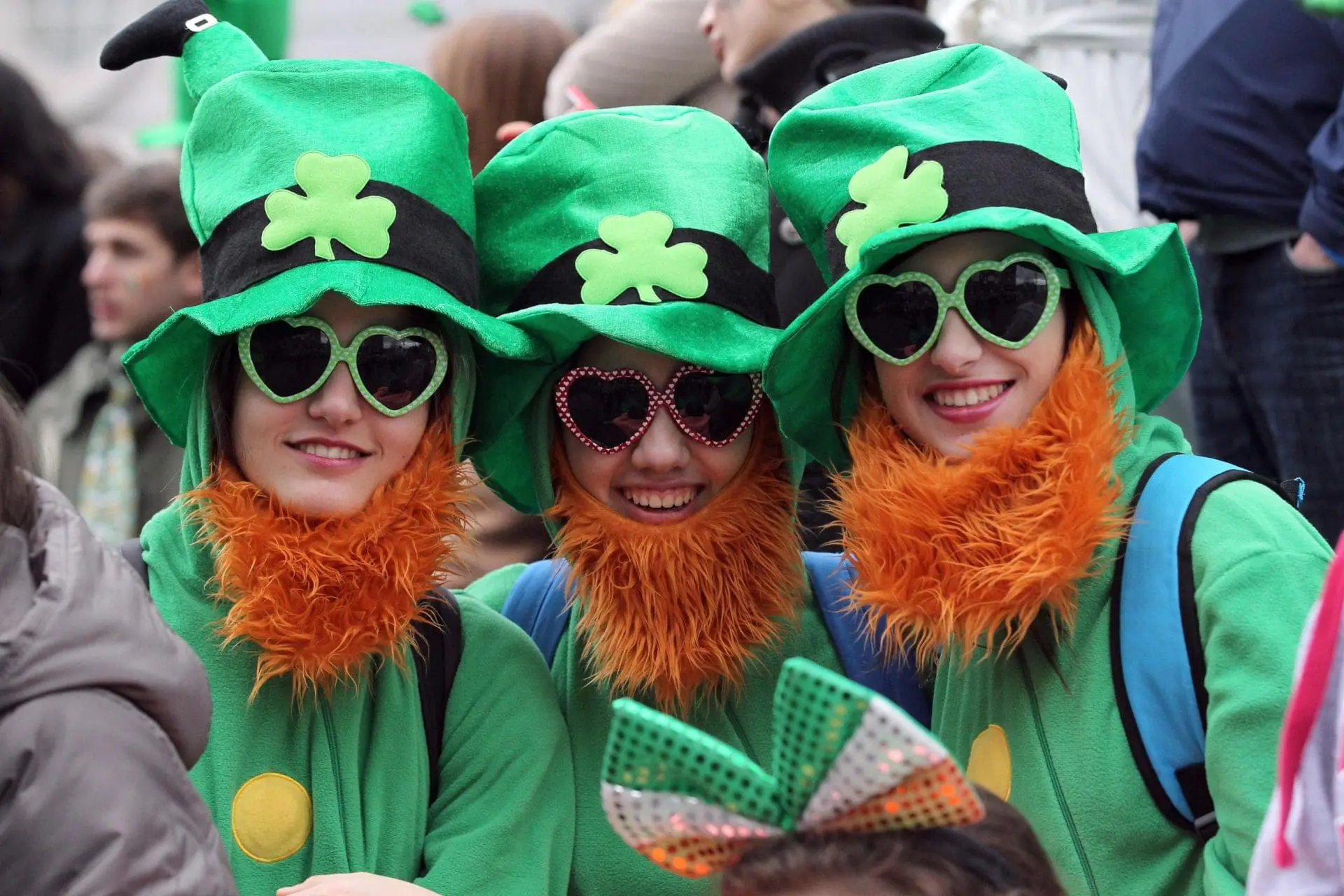 Photo of Three individuals wearing green costumes with shamrock designs and orange beards, smiling at the camera. | Wander Sober