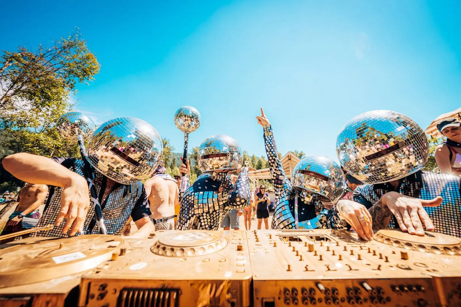 Photo of Performers wearing mirror ball helmets and sequined outfits interacting with a DJ setup outdoors. | Wander Sober