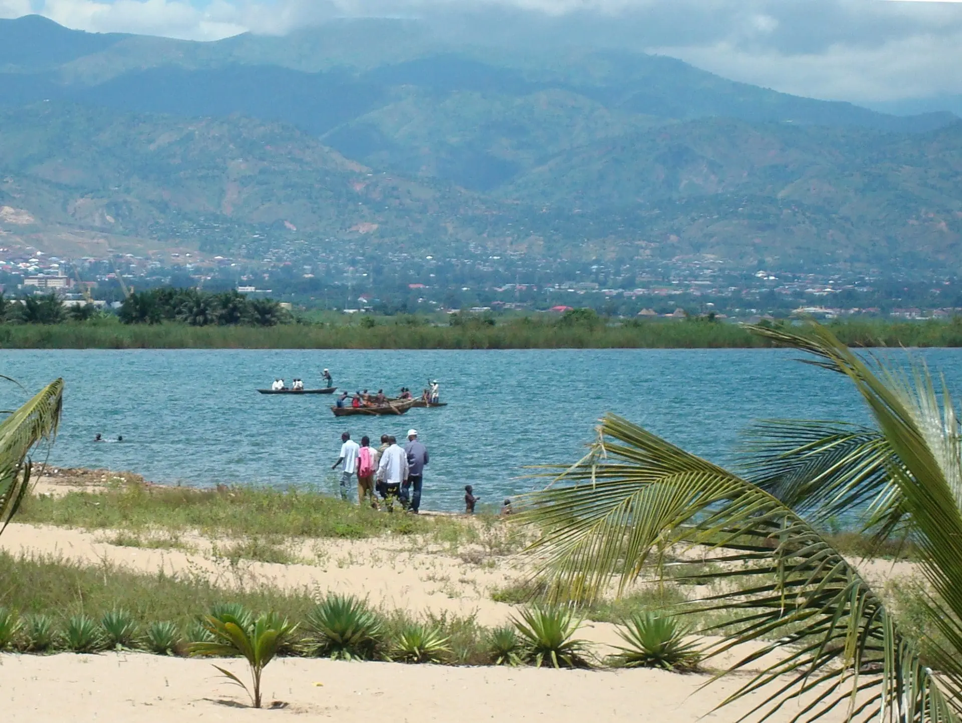Photo of Group of people walking along the shore near a body of water with a boat in the background. | Wander Sober