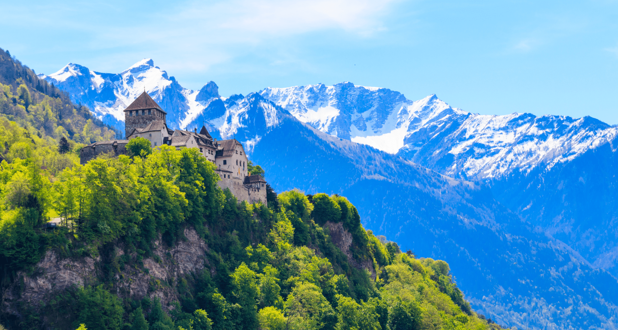 Photo of A castle situated on a mountain ridge with snow-capped peaks in the background. | Wander Sober