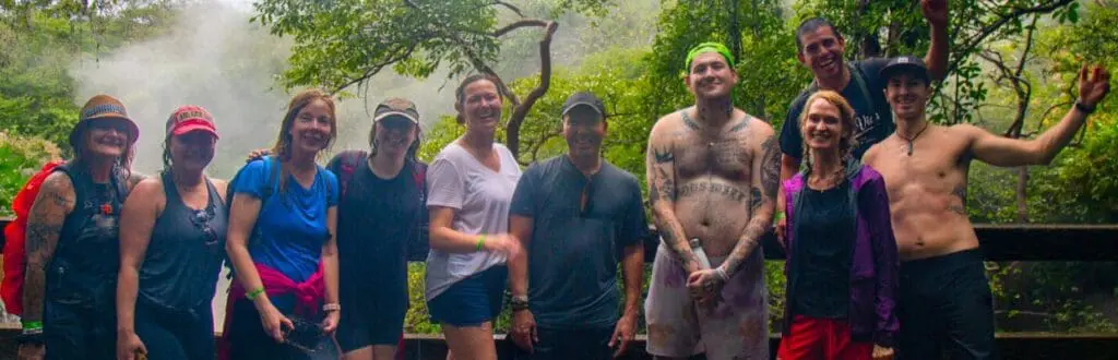 Photo of A group of ten individuals posing together in a forested area with greenery and mist in the background. | Wander Sober
