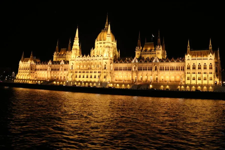 Photo of Hungarian Parliament Building illuminated at night along the Danube River in Budapest. | Wander Sober