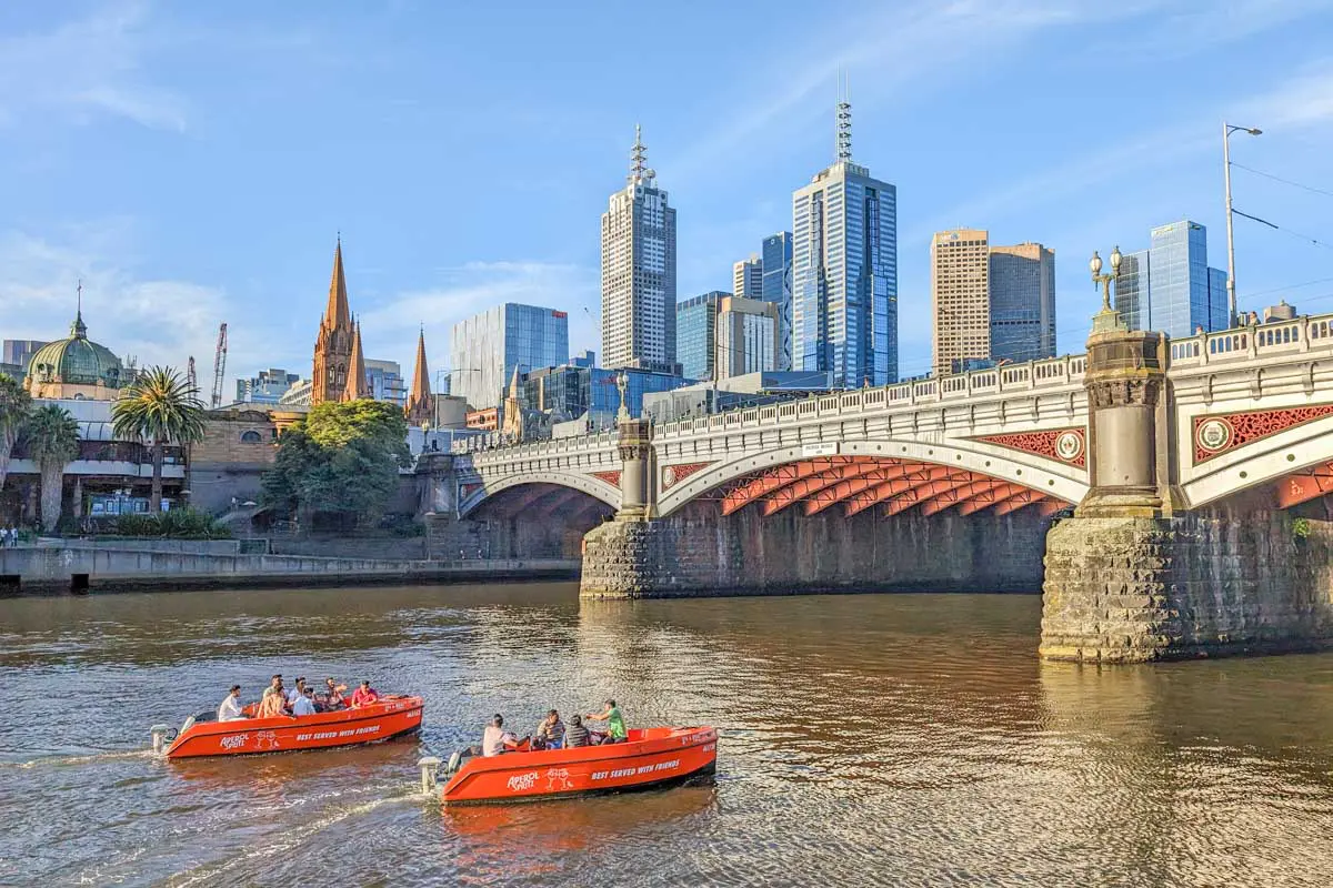 Discover Free Things to Do in Melbourne: Your Ultimate Guide to Fun and Culture Photo of Two orange boats with passengers navigating the Yarra River in Melbourne, with city skyline in the background. | Wander Sober