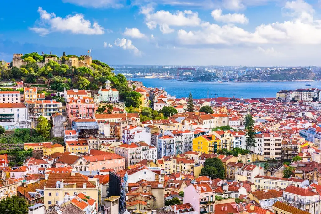 Photo of Aerial view of Lisbon showcasing red-roofed buildings and a castle on a hilltop. | Wander Sober