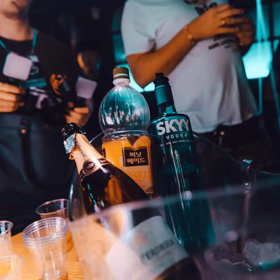 Photo of A collection of alcohol bottles including champagne and vodka in an ice bucket with plastic cups nearby. | Wander Sober