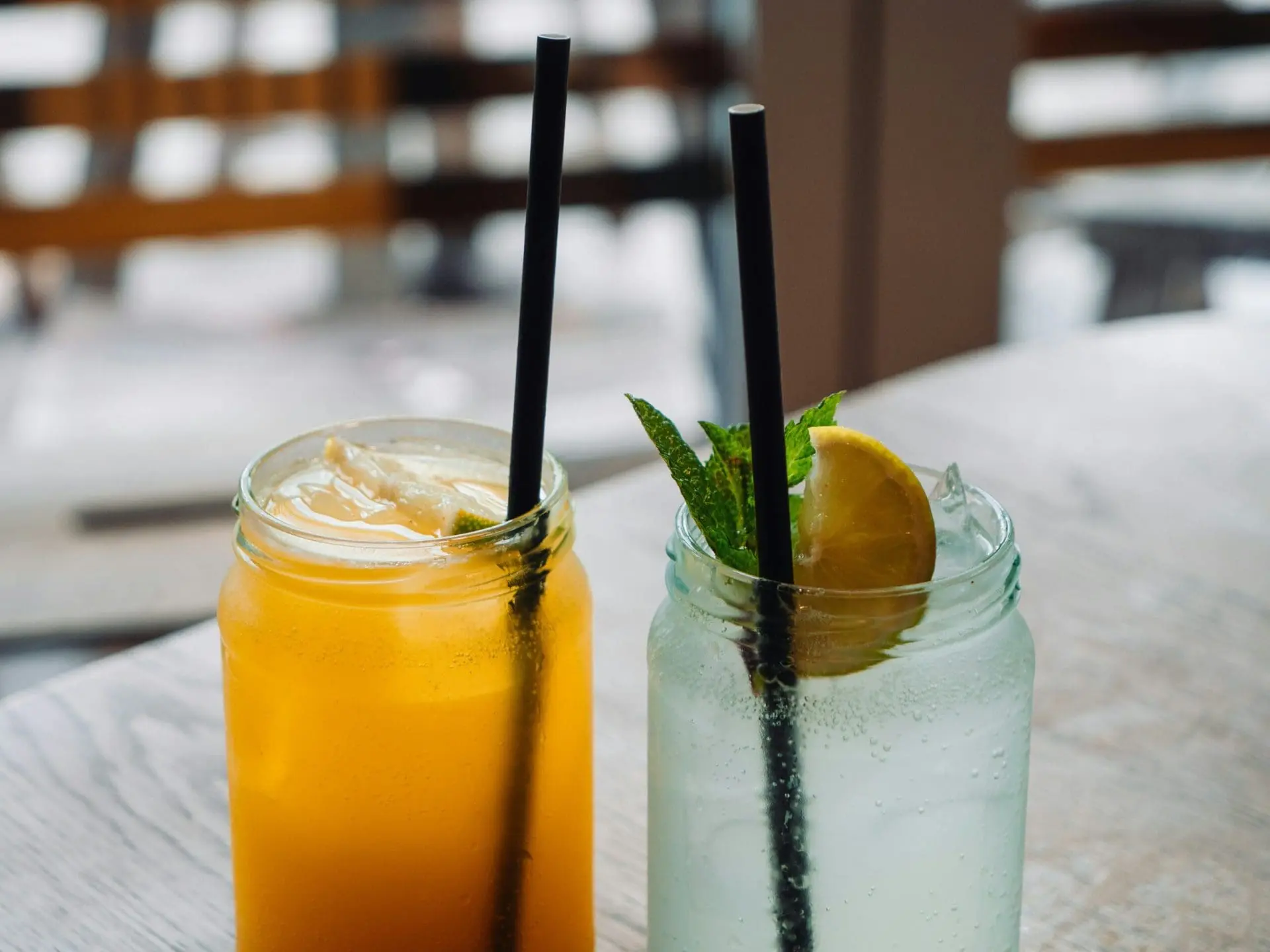 Photo of Two glasses with drinks, one orange and one clear, each with a straw and garnished with lemon and mint. | Wander Sober