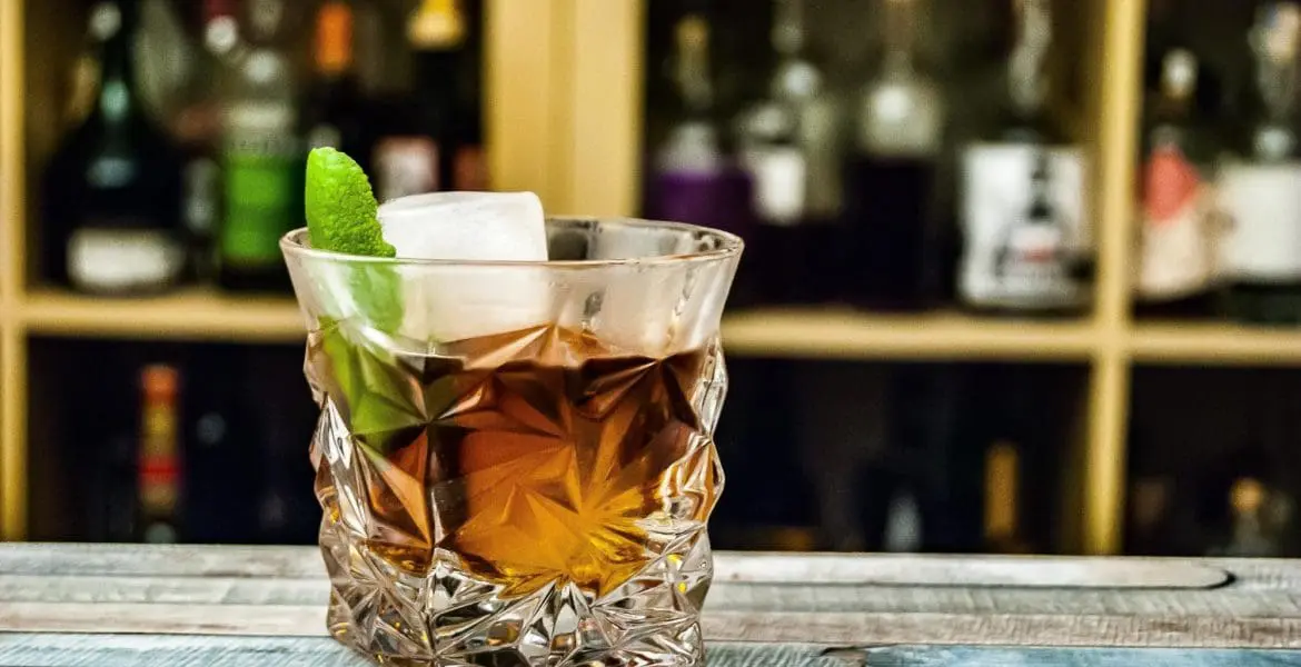 Photo of A whiskey cocktail served in a crystal glass with ice and a lime wedge. | Wander Sober