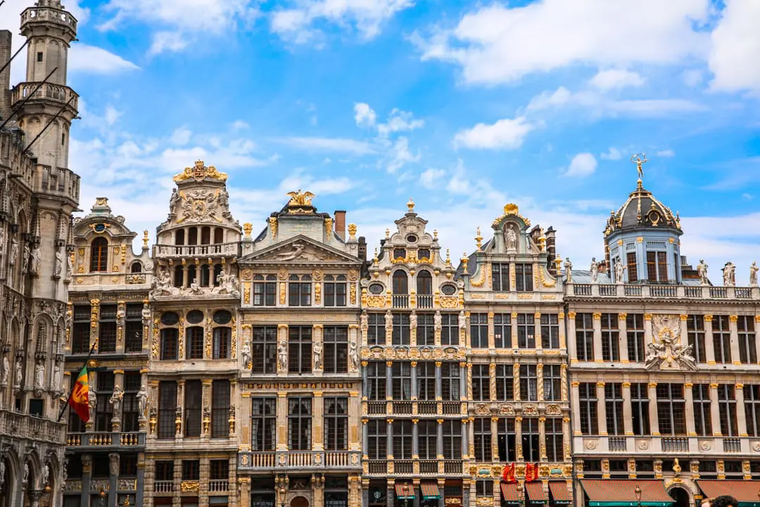 Photo of Row of ornate historic buildings with intricate architectural details in Brussels under a blue sky. | Wander Sober