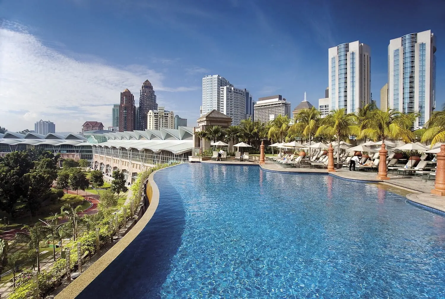 Photo of Infinity pool with clear blue water at a high-rise hotel surrounded by palm trees and city skyline. | Wander Sober