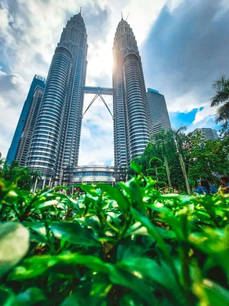 Photo of View of the Petronas Twin Towers from below, surrounded by greenery and blue sky. | Wander Sober