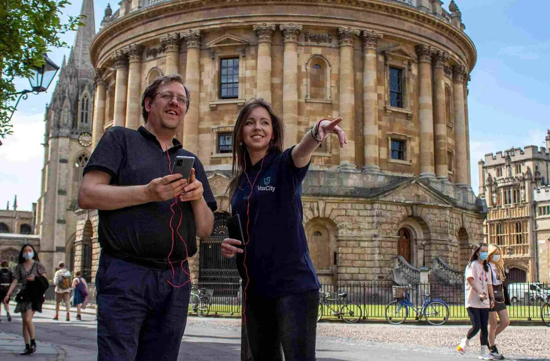 Photo of Two individuals standing outside a historic building, one pointing while the other holds a smartphone. | Wander Sober