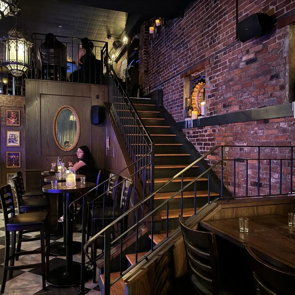 Photo of Interior view of a bar featuring wooden stairs, seating areas, and exposed brick walls. | Wander Sober
