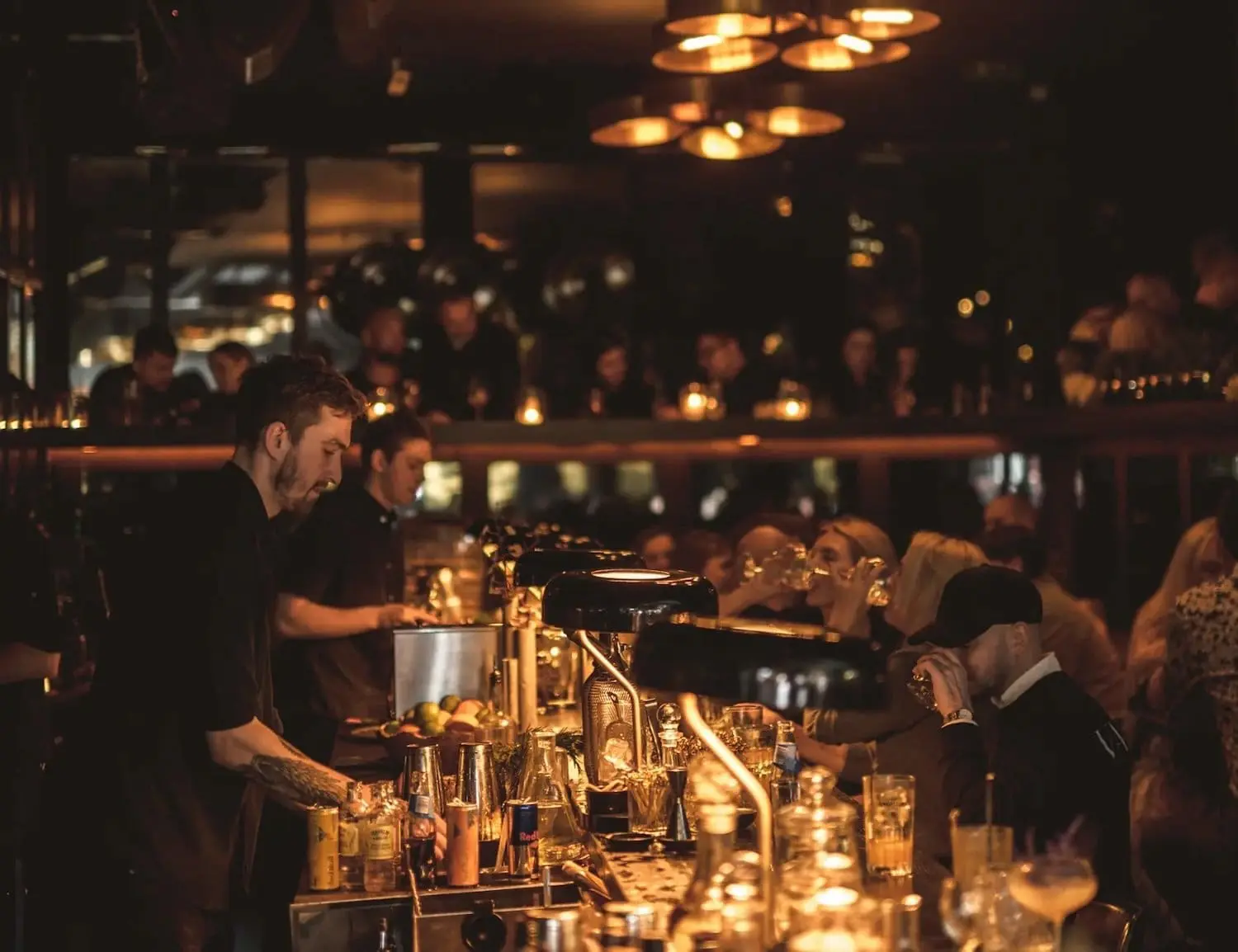 Photo of Bartender mixing drinks at a bar with patrons seated in the background. | Wander Sober