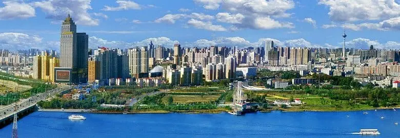 Photo of Panoramic view of a city skyline with modern buildings and a river in the foreground. | Wander Sober