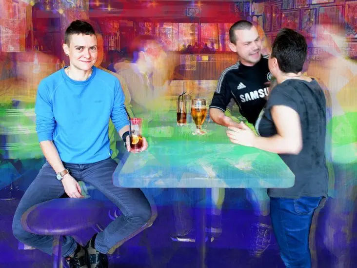 Photo of Three individuals seated at a table in a bar, one person is looking at the camera while the others are engaged in conversation. | Wander Sober