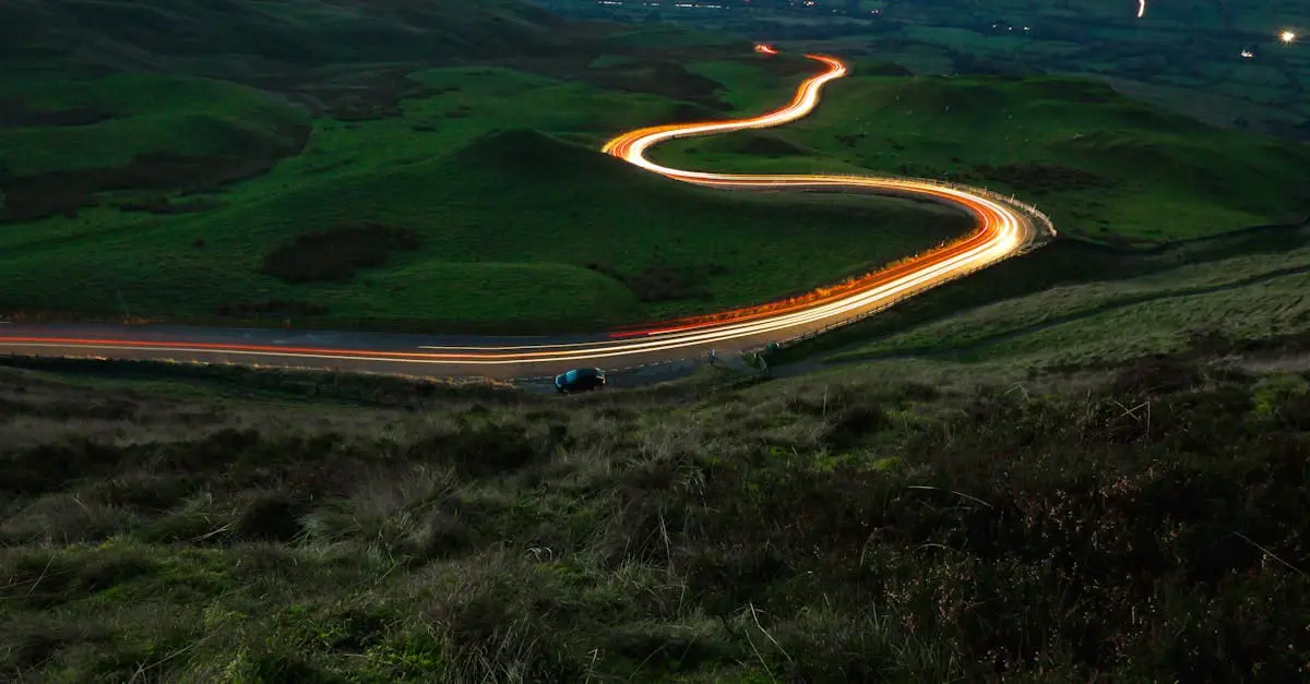 Photo of A winding road illuminated by vehicle headlights at night, surrounded by green hills. | Wander Sober