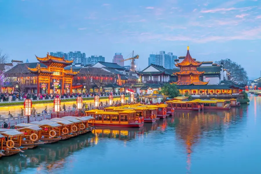 Photo of View of Qingdao's waterfront featuring traditional boats and illuminated buildings along the river. | Wander Sober