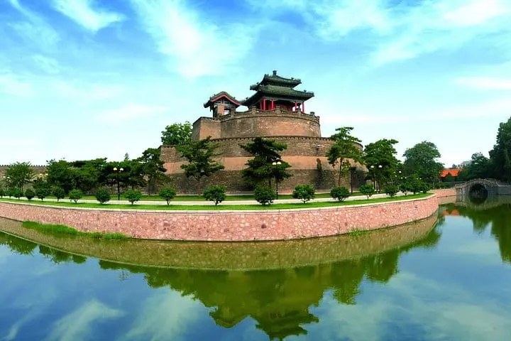 Photo of A panoramic view of an ancient Chinese fortress surrounded by water and greenery. | Wander Sober