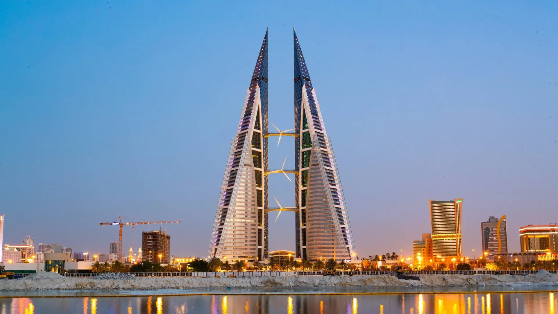Photo of Bahrain World Trade Center towers illuminated at dusk with a clear sky in the background. | Wander Sober