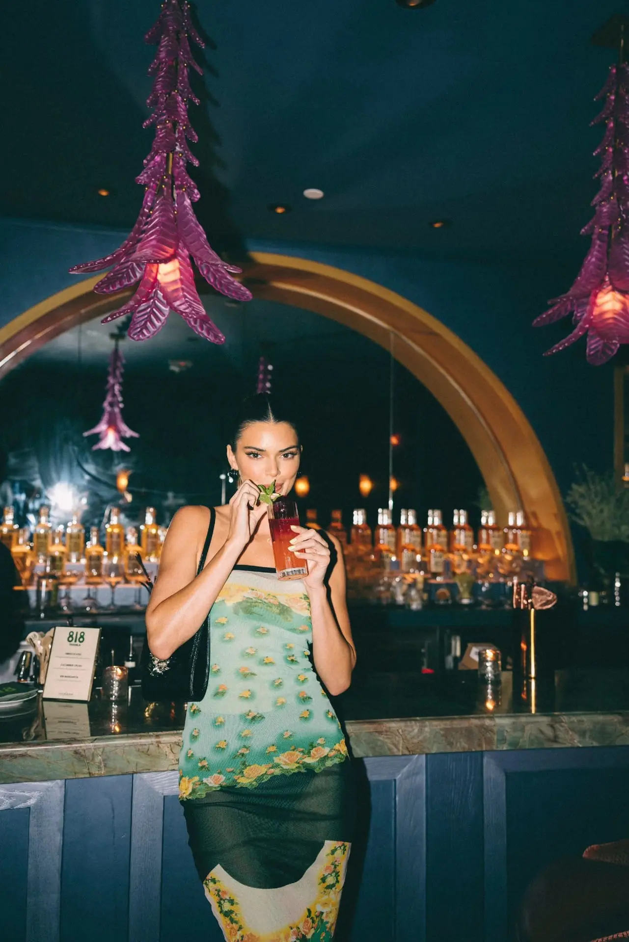 Photo of Woman holding a drink while wearing a floral dress at a bar with decorative lighting. | Wander Sober