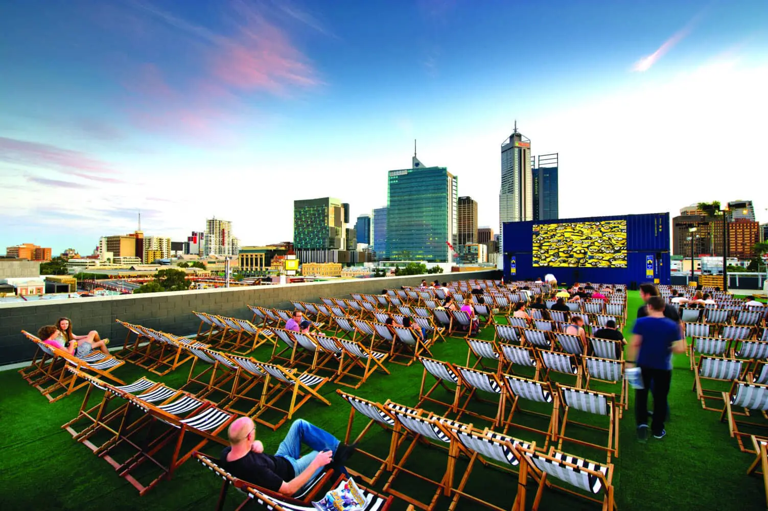 Photo of Outdoor cinema setup with deck chairs arranged in rows on a rooftop with a city skyline in the background. | Wander Sober