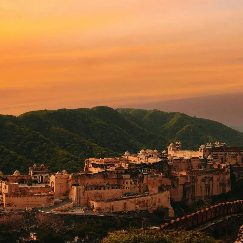 Photo of Amber Fort located in Rajasthan, India, with a backdrop of mountains during sunset. | Wander Sober